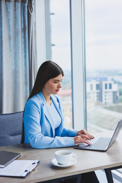 Young beautiful business woman in a blue shirt sitting in the office with a laptop and doing business