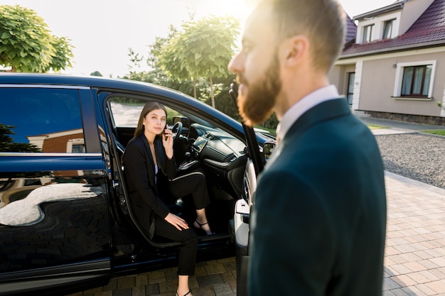 Young beautiful business woman getting out the front door of her car. Driver or business partner helping woman to get out of the car