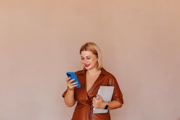 Young beautiful businesswoman in a brown dress talking on the phone with a laptop in her hands Young