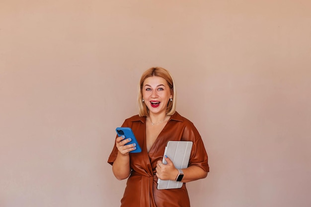 Young beautiful businesswoman in a brown dress talking on the phone with a laptop in her hands Young