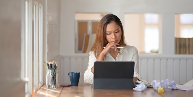 Young beautiful businesswoman concentrated in her work while using digital tablet in office room