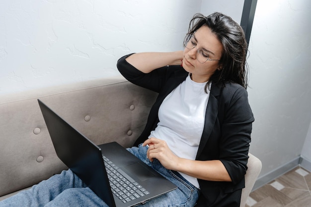 A young and beautiful businesswoman tired of work a girl working at her laptop at home rubbing her t