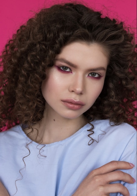 Young beautiful caucasian model with curly hairstyle wearing blue blouse on magenta background