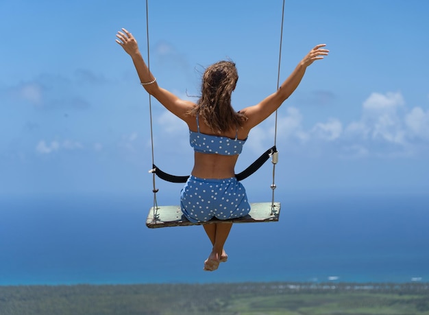 Young beautiful caucasian woman on the rope swing with sea and sky background concept of vacation an...