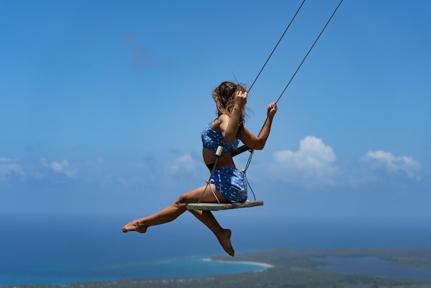 Young beautiful caucasian woman on the rope swing with sea and sky background concept of vacation an...