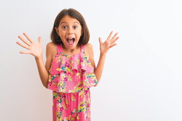 Young beautiful child girl wearing pink floral dress standing over isolated white background celebrating crazy and amazed for success with arms raised and open eyes screaming excited Winner concept