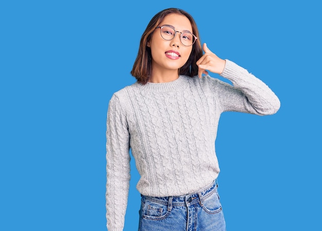 Young beautiful chinese girl wearing casual clothes smiling doing phone gesture with hand and fingers like talking on the telephone. communicating concepts.