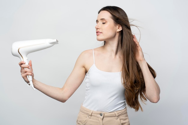 Young beautiful confident woman using hair dryer isolated on white background