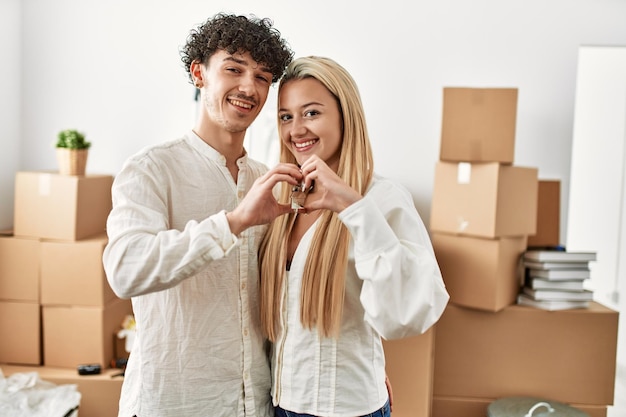 Young beautiful couple doing heart symbol with fingers and holding key of new home