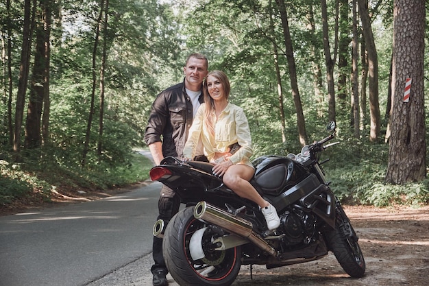 Young beautiful couple hugging sitting on a motorcycle travel together on a forest road