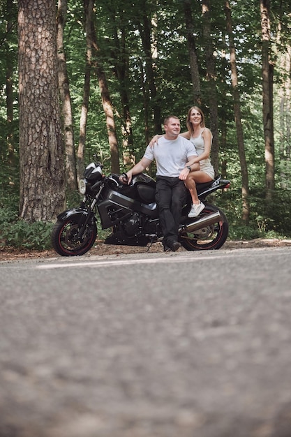 Young beautiful couple hugging sitting on a motorcycle travel together on a forest road