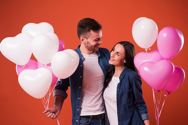 Young beautiful Couple in love are posing together with colorful balloons in casual wear while celebrating St. Valentine's day.