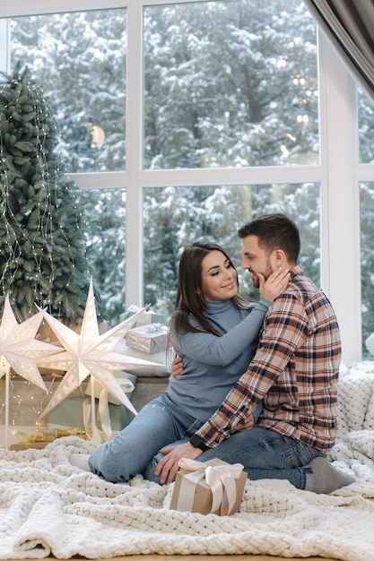 Young and beautiful couple of man and woman sitting in front of big windor its snow outside happy