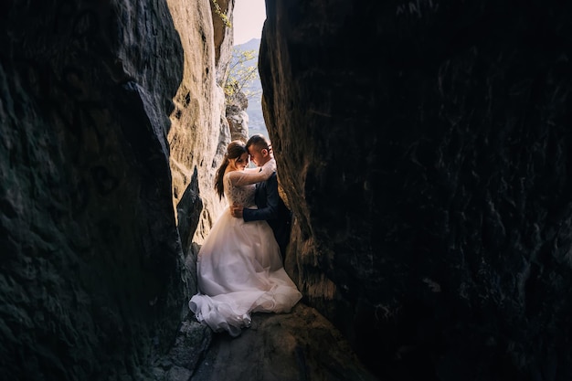 Young beautiful couple of man and woman in wedding dress and suit huggingbetween the crevices of high stone mountains