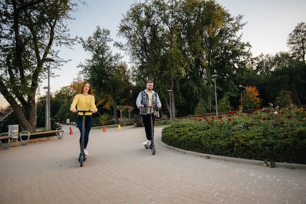 A young beautiful couple rides electric scooters in the Park on a warm autumn day