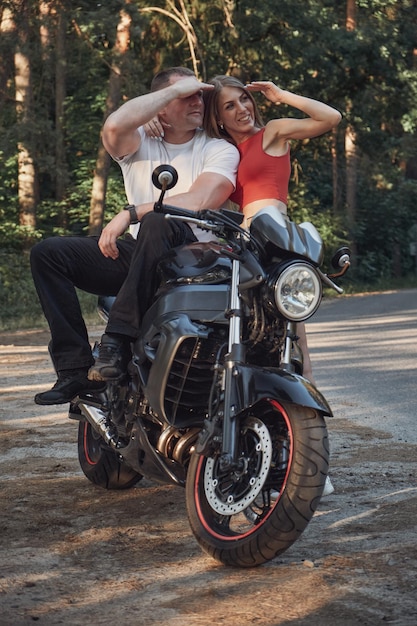 Young beautiful couple talking and having fun sitting on a motorcycle traveling together on a forest