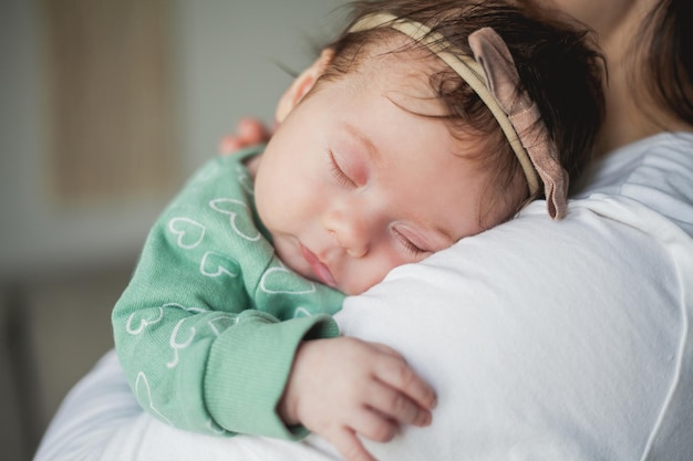 Young beautiful darkhaired mother holds her newborn daughter in her arms in a cozy home Family portrait Motherhood Young woman kisses her 2 month old baby