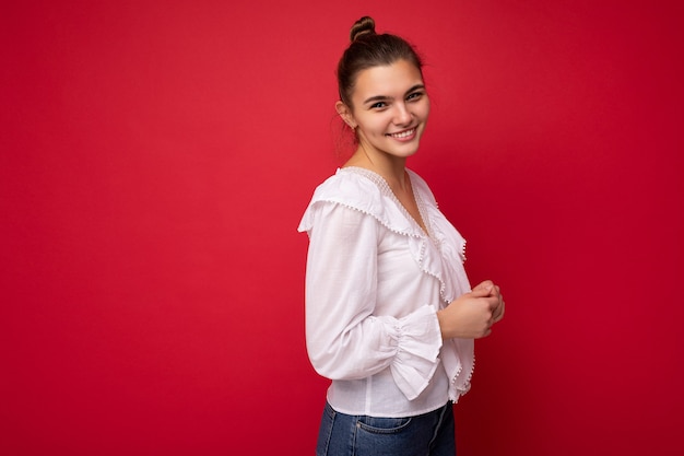 Young beautiful european stylish brunette woman wearing white blouse isolated over red wall with positive sincere emotions.