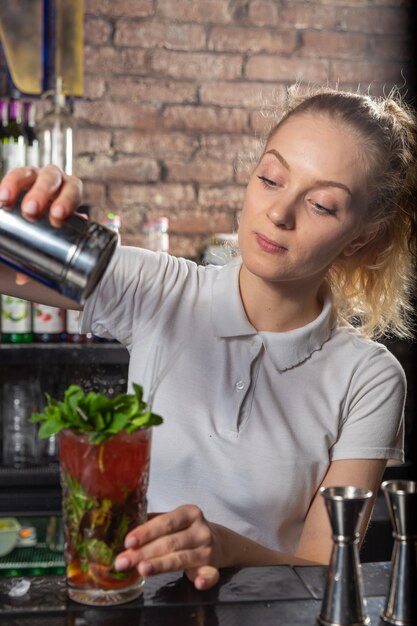 Young beautiful female bartender sprinkles the cocktail with powdered sugar