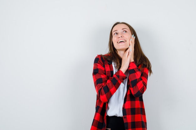 Young beautiful female in casual outfit with hand on cheek, looking away and looking cheerful , front view.