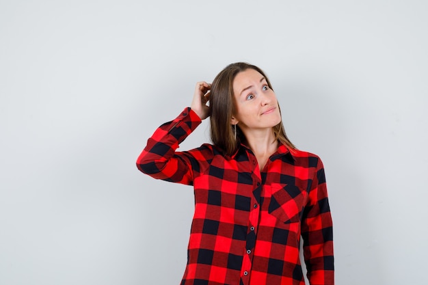 Young beautiful female in casual shirt scratching her head, looking away and looking curious , front view.