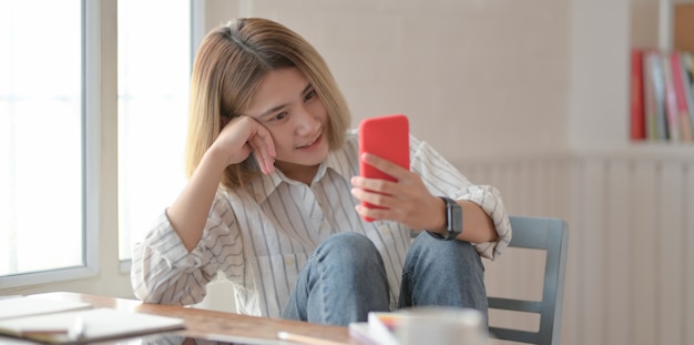 Young beautiful female designer looking at smartphone and sitting on the chair