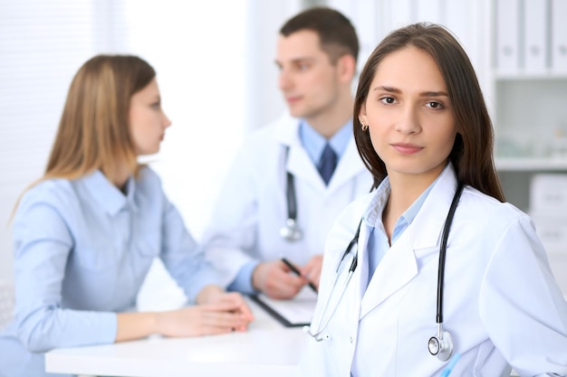 Young beautiful female doctor smiling  on the background with patient  in hospital. High level and quality medical service concept.