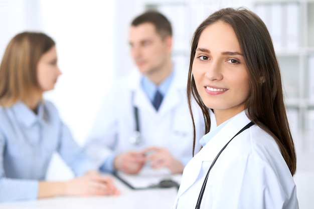 Young beautiful female doctor smiling  on the background with patient  in hospital. High level and quality medical service concept.