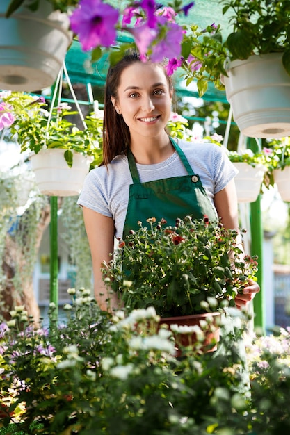 Young beautiful female florist posing, smiling among flowers.