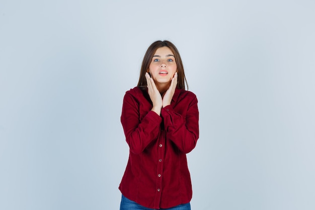 Young beautiful female holding hand near face in shirt and looking confident