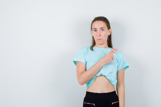 Young beautiful female pointing at upper right corner in t-shirt and looking perplexed. front view.