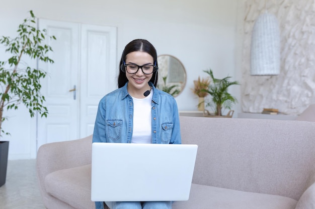 Young beautiful female student studying online at home with laptop on in headphones he sits on the