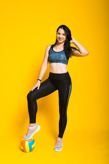 Young beautiful female volleyball player isolated on yellow in studio