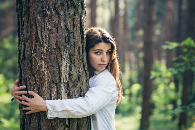 Young beautiful female volunteer hugs a tree with love in the forest