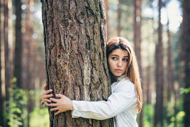 Young beautiful female volunteer hugs a tree with love in the forest