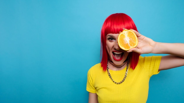 A young beautiful funny model with a slice of orange near her eyes in the background with makeup hairstyle Bright funny summer photo Bright background A place for your text