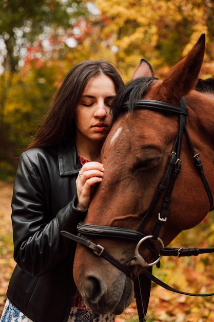 Young beautiful girl in an autumn park stroking a horse and walking with her