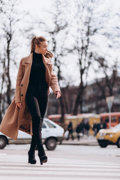 A young beautiful girl in a beige coat crosses the road. clothing advertisement