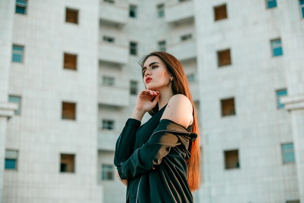 Young beautiful girl in a black jacket  poses near a high white house.