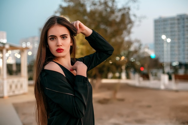 Young beautiful girl in a black jacket with a scarf posing in the evening on the street.