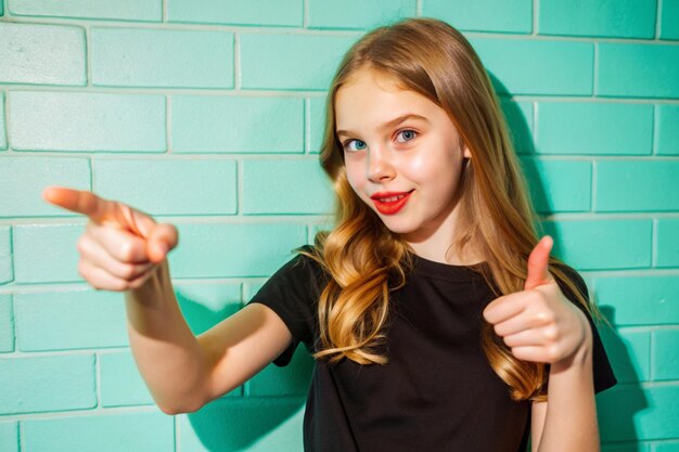 Photo young beautiful girl in black tshirt pointing fingers in side over white wall