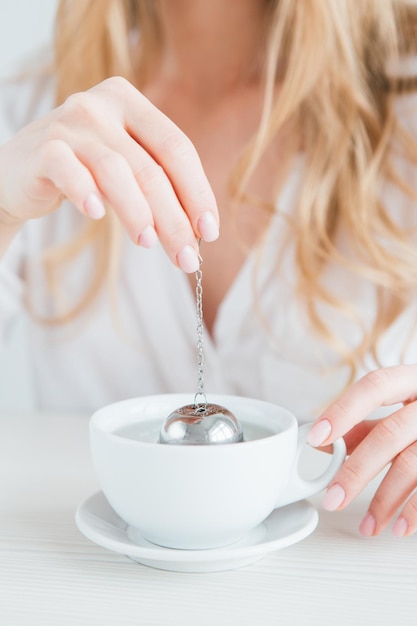 Young beautiful girl brews tea in a useful reusable metal strainer. Hands and Cup close-up. The concept of zero waste. Toning.