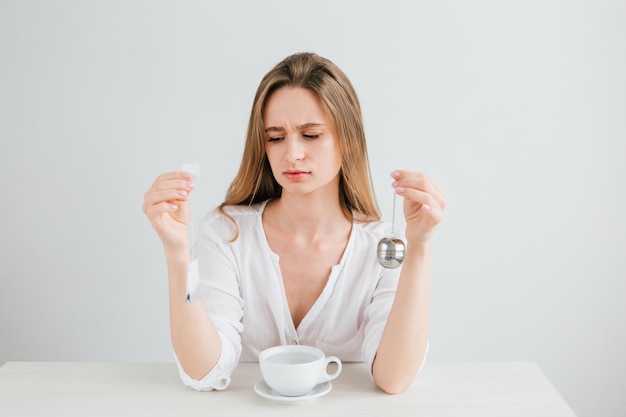 Young beautiful girl compares a useful reusable metal tea strainer with a harmful tea bag. The concept of zero waste. Toning.