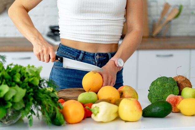 Young beautiful girl cuts fresh orange to prepare fresh juice in the kitchen