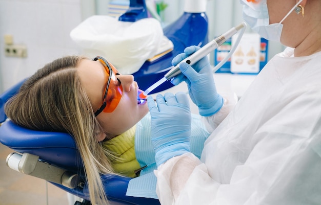 A young beautiful girl in dental glasses treats her teeth at the dentist with ultraviolet light filling of teeth