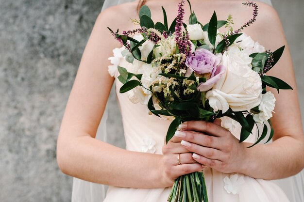 Young beautiful girl in elegant dress is standing and holding hand bouquet of pastel pink flowers and greens at nature The bride holds a wedding bouquet outdoors