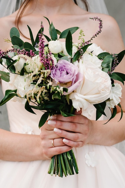 Young beautiful girl in elegant dress is standing and holding hand bouquet of pastel pink flowers and greens at nature The bride holds a wedding bouquet outdoors