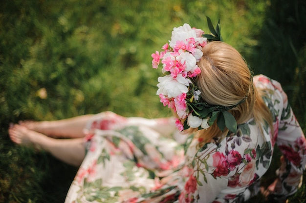 Young and beautiful girl in a flower diadem sitting on the grass