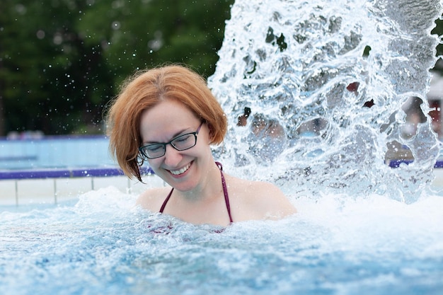 Young beautiful girl in glasses bathes in a pool under the stream of water