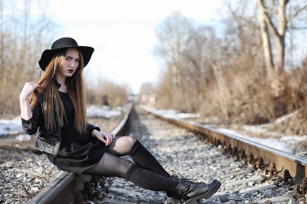 Young beautiful girl in a hat and with a dark make-up outside. Girl in the Gothic style on the street. A girl walks down the city street in a leather waistcoat with phone.